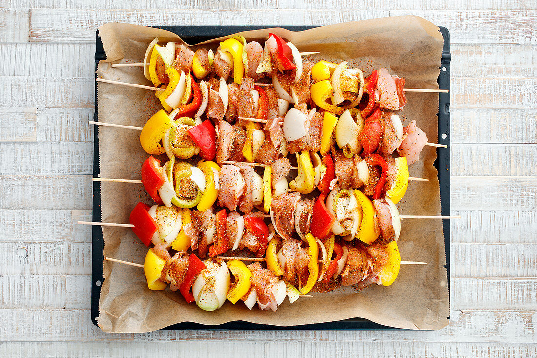 Raw chicken skewers with peppers and onions on a baking tray (seen from above)