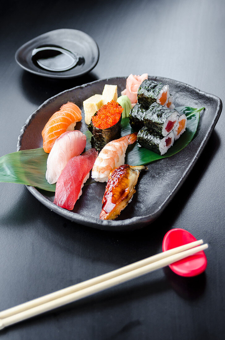 Japanese fresh mixed sushi platter with salmon, tuna, yellowtail, shrimp nigiri, salmon maki, tuna maki on a black plate and black table