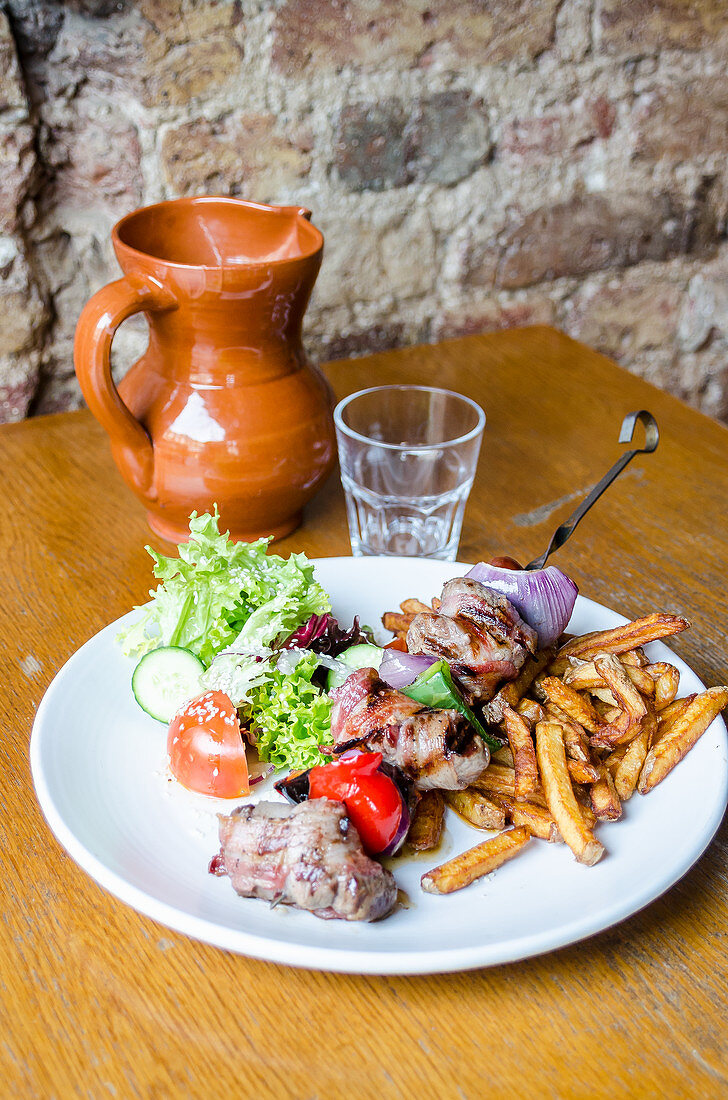 Skewer of beef fillet with bacon, red pepper, red onion, spanish sausage served with golden chips and fresh salad