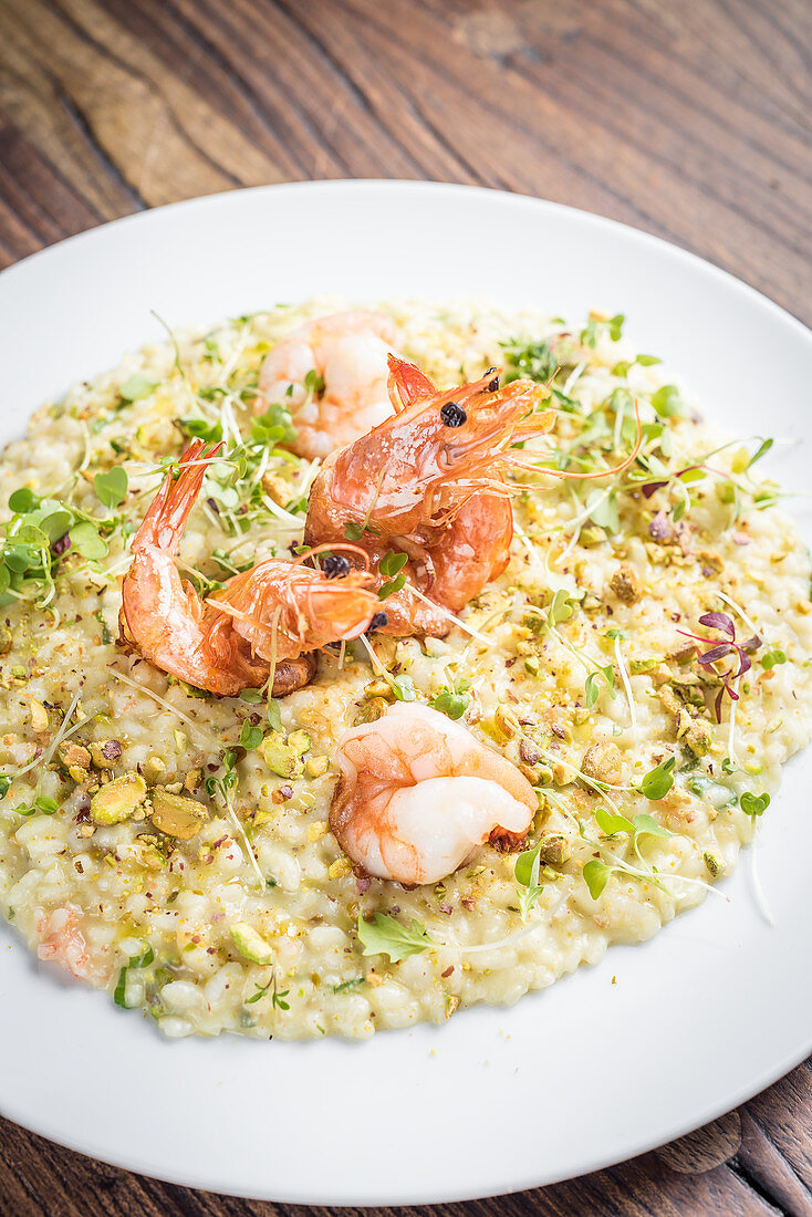 Sicilian pistachio and king prawns risotto with herbs on a white plate and a wooden background