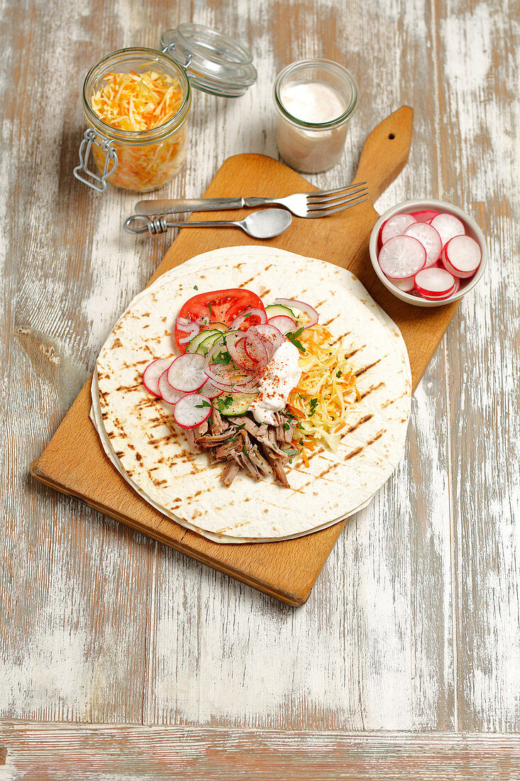 A tortilla topped with pork, coleslaw and vegetables
