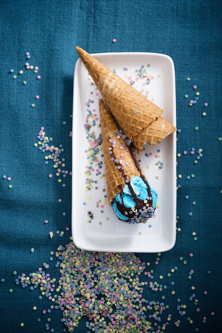 Blue vegan ice cream with chocolate sauce and sugar confetti in cones