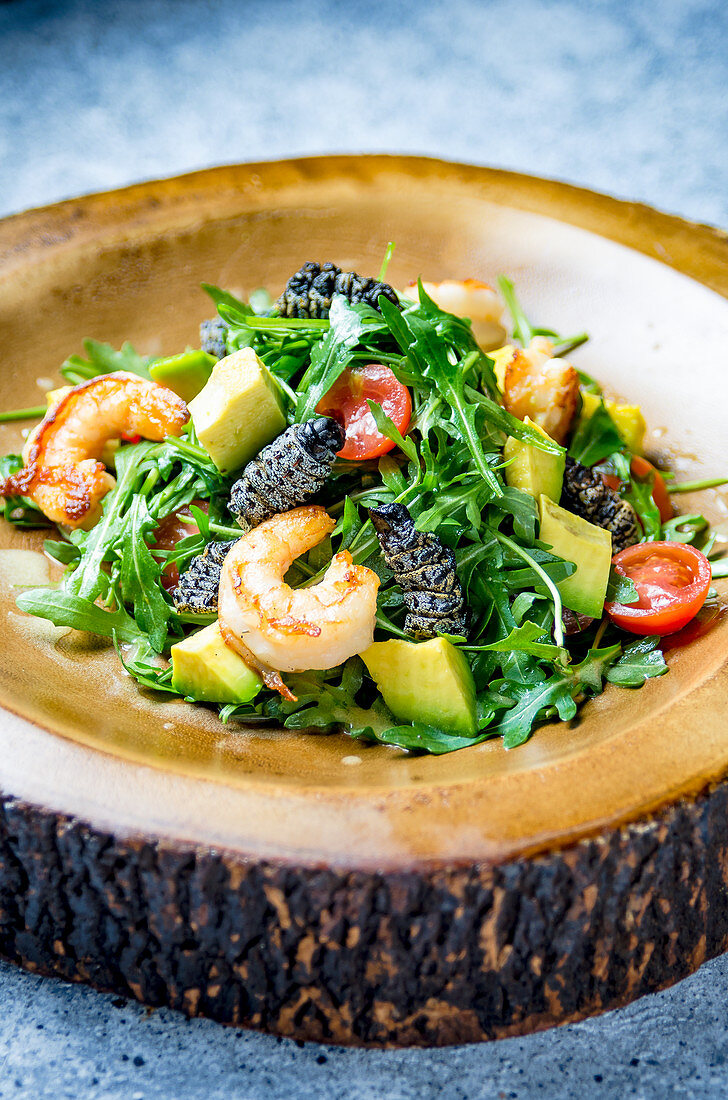 Rocket salad with caterpillars and prawns, avocado, cherry tomatoes on a wooden plate and marble background