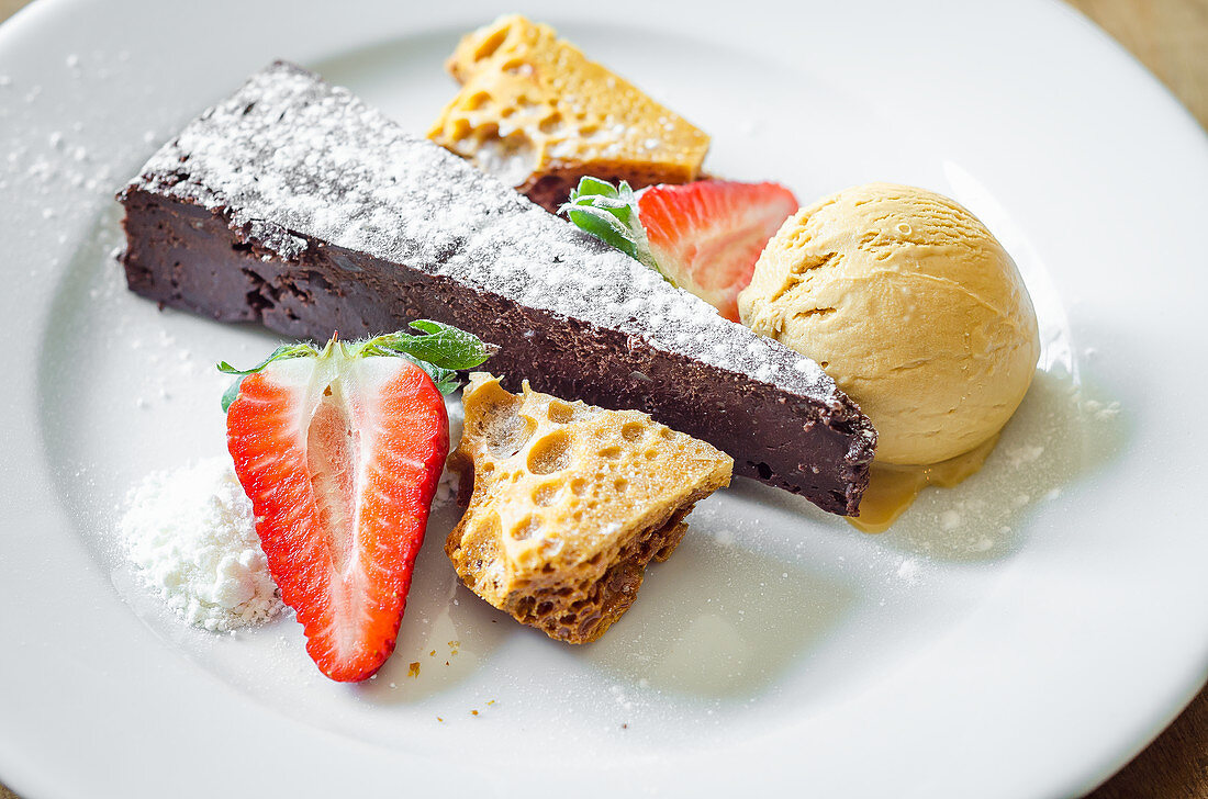 Moist and rich chocolate and honeycomb cake served with honeycomb, ice cream and fresh strawberries decorated with icing sugar