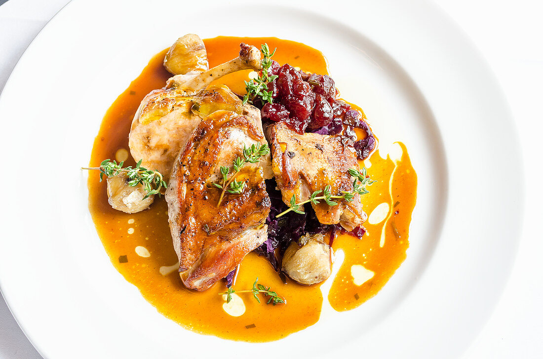 Confit of duck breast with cranberry sauce compote and cabbage in a red wine and juices sauce on a white plate