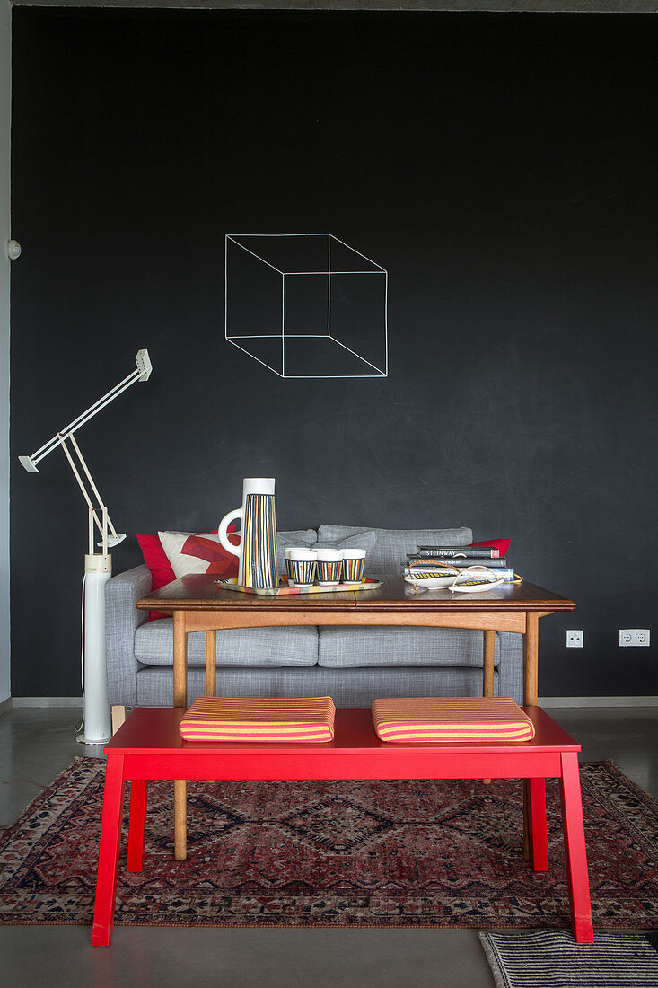 Rote Bank, Holztisch und Sofa vor Tafelwand
