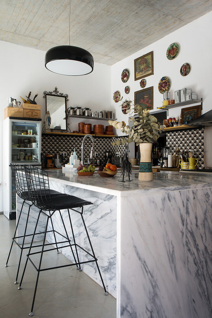 Marble island counter and classic barstools below concrete ceiling