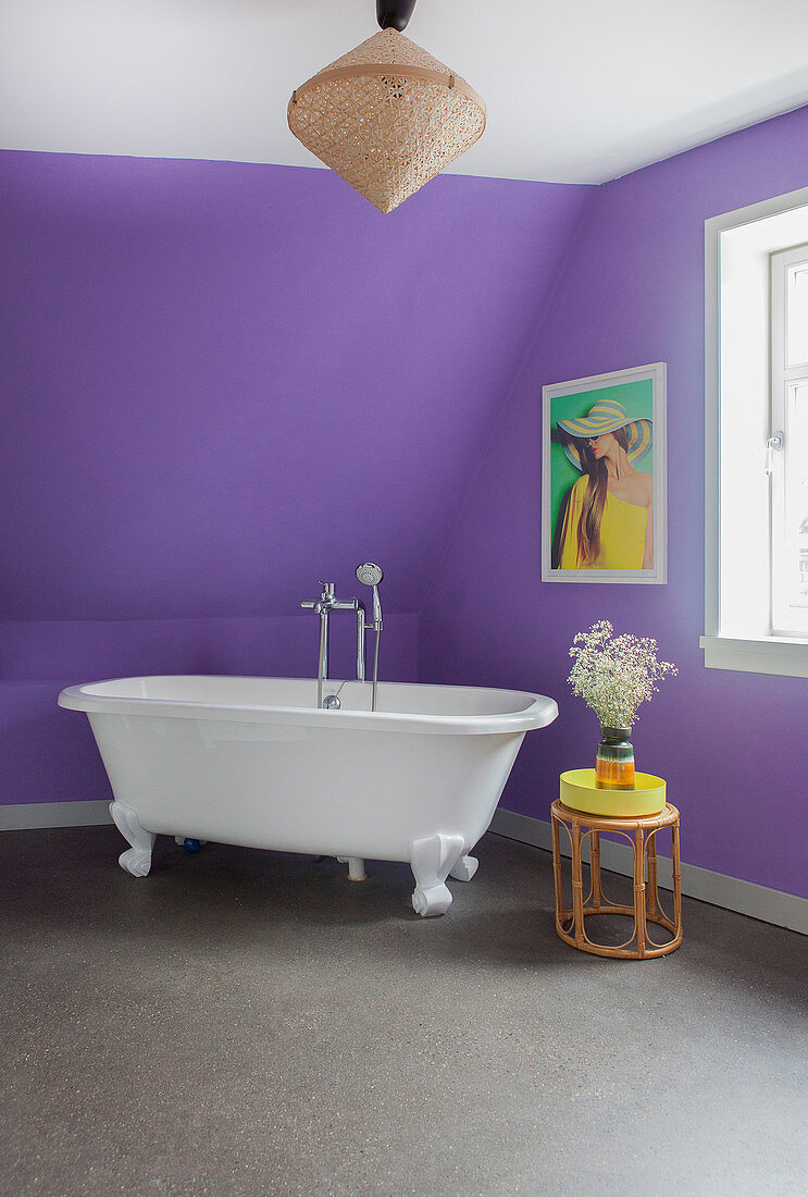 Free-standing bathtub below sloping ceiling in purple bathroom