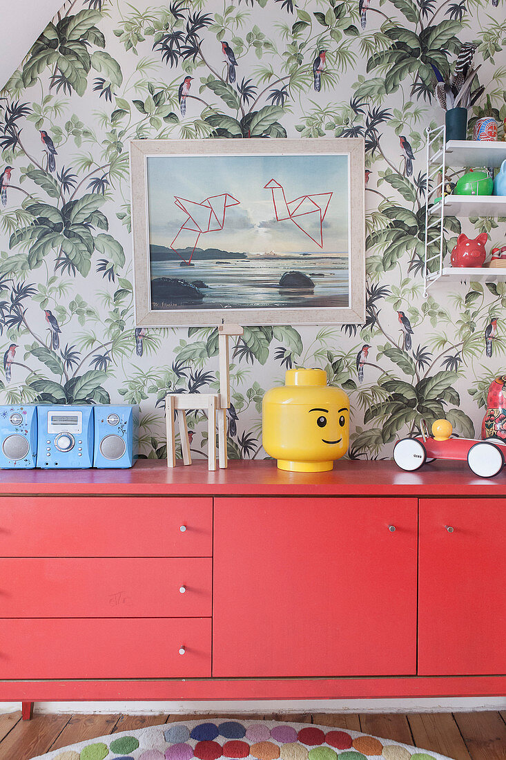 Red sideboard against jungle-patterned wallpaper in child's bedroom