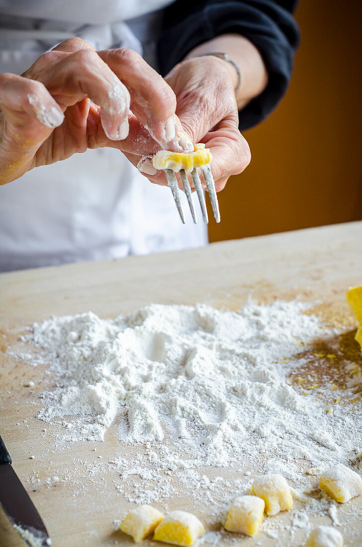 Italian chef making fresh homemade gnocchi pasta rolling on a fork and flour on the wooden board