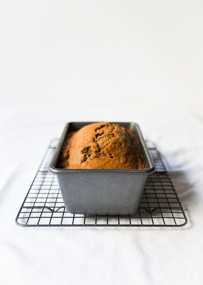 Banana bread cooling in a loaf tin against a white background