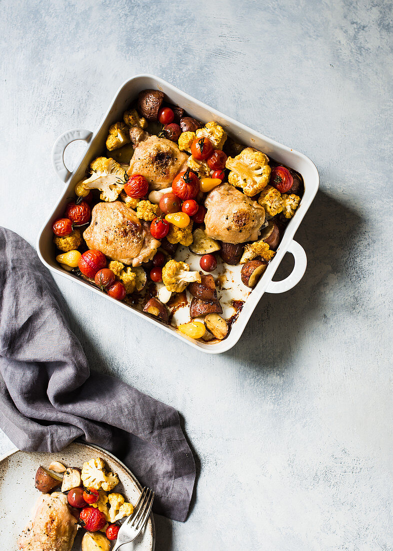 Roasted chicken drumsticks with vegetables in an oven dish (top view)