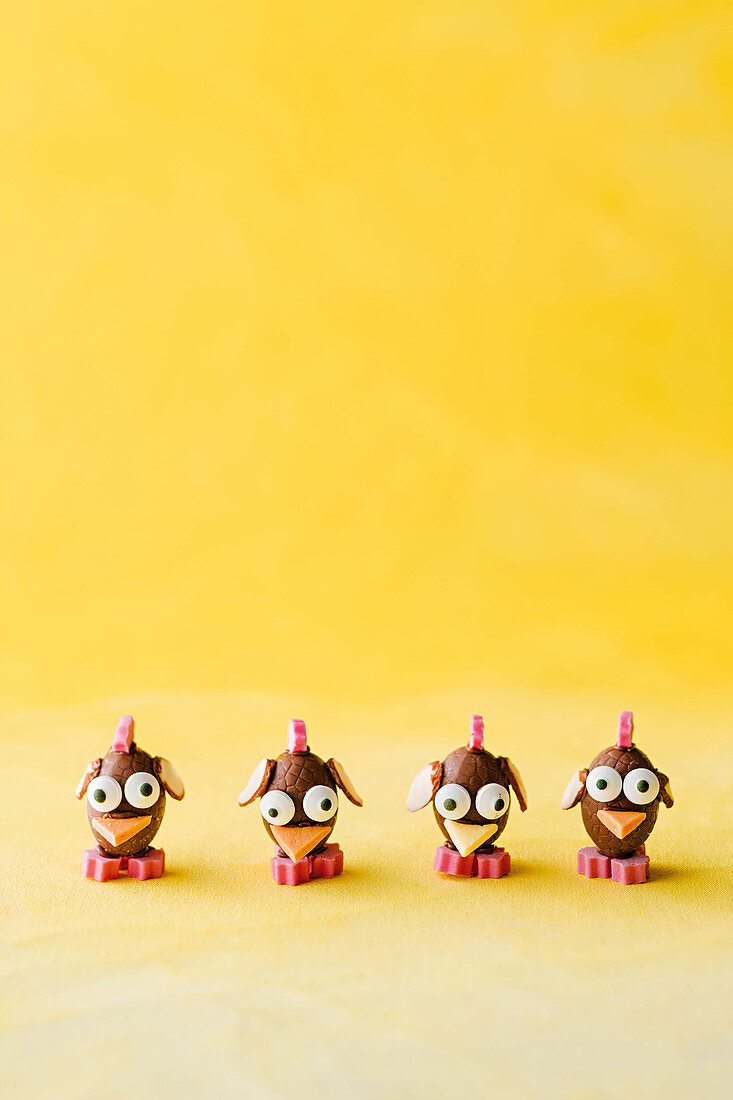 Comical chicks made of chocolate easter eggs against a yellow background