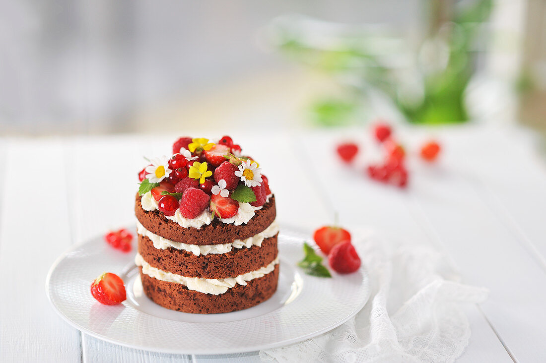 A mini naked cake with chocolate sponge, white chocolate cream, fresh berries and flowers (vegan)