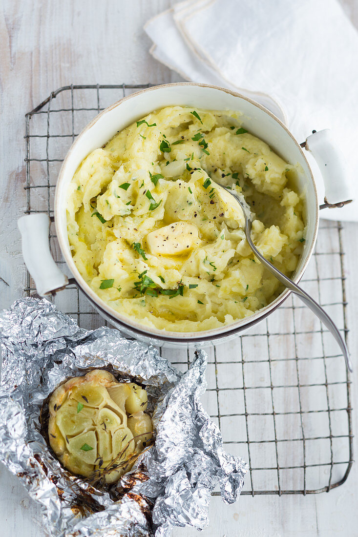 Hausgemachtes Kartoffelpüree mit Butter in Topf und gebackener Knoblauch