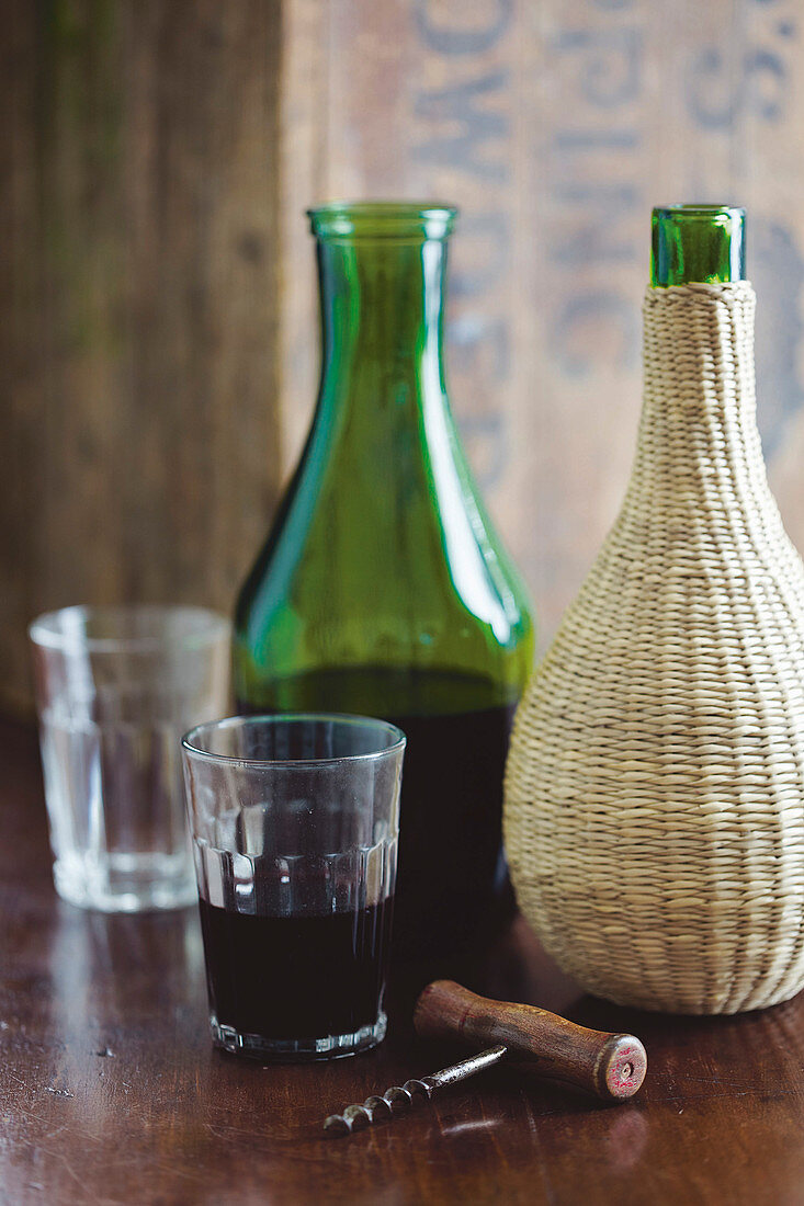Rotwein in grüner Karaffe und in einer Korbflasche