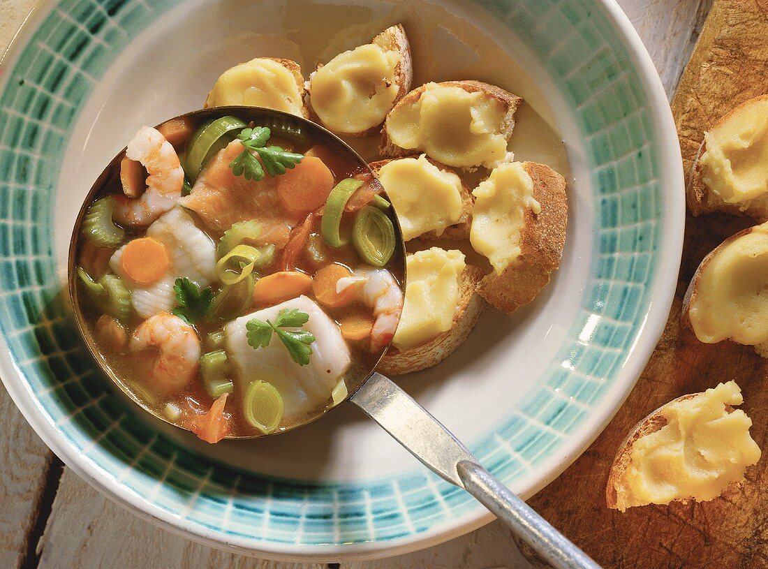 A Ladle of Fish Soup Over a Bowl with Croutons