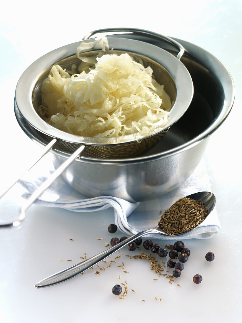 Sauerkraut im Sieb, davor verschiedene Gewürze