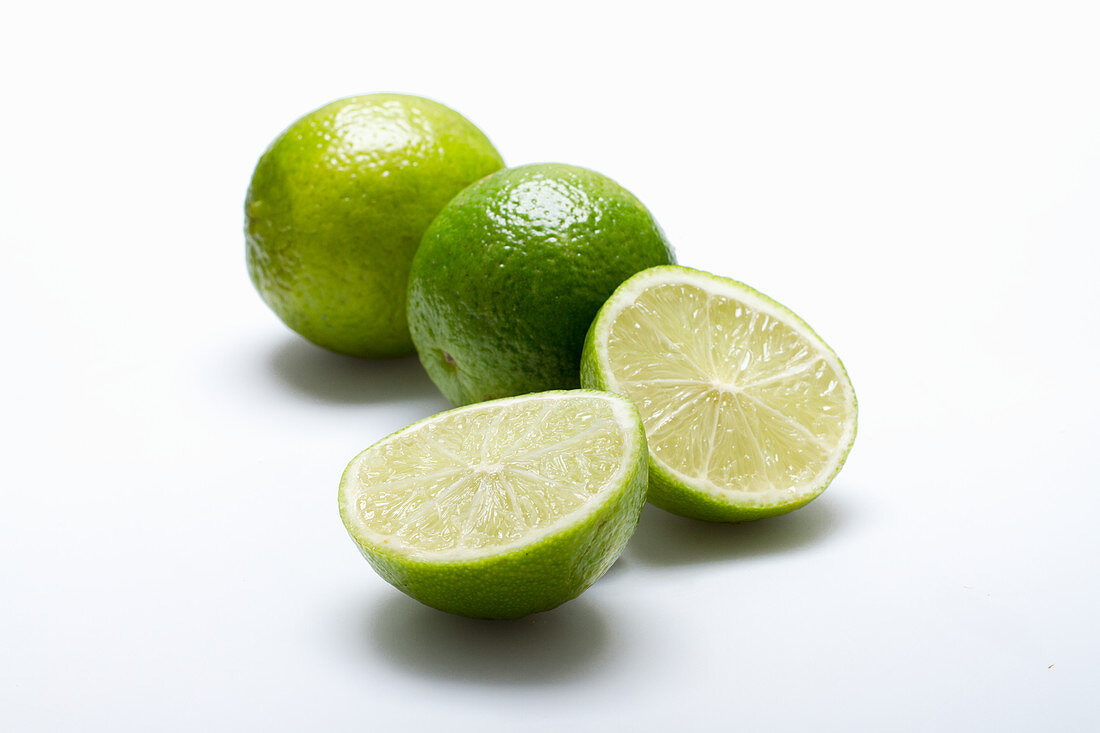 Three limes, one halved, on a white surface