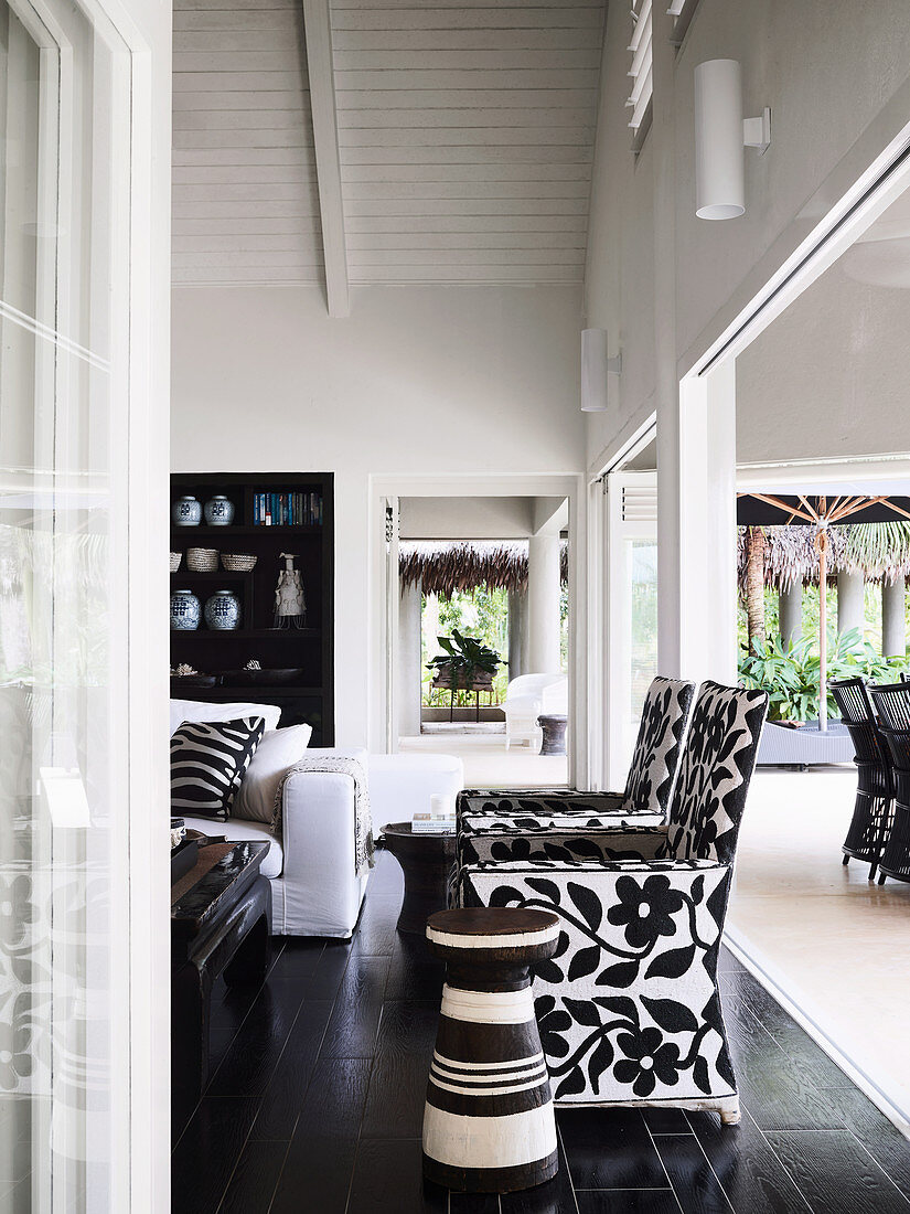 Open living space in black and white, designer armchairs and sofa in front of the terrace opening