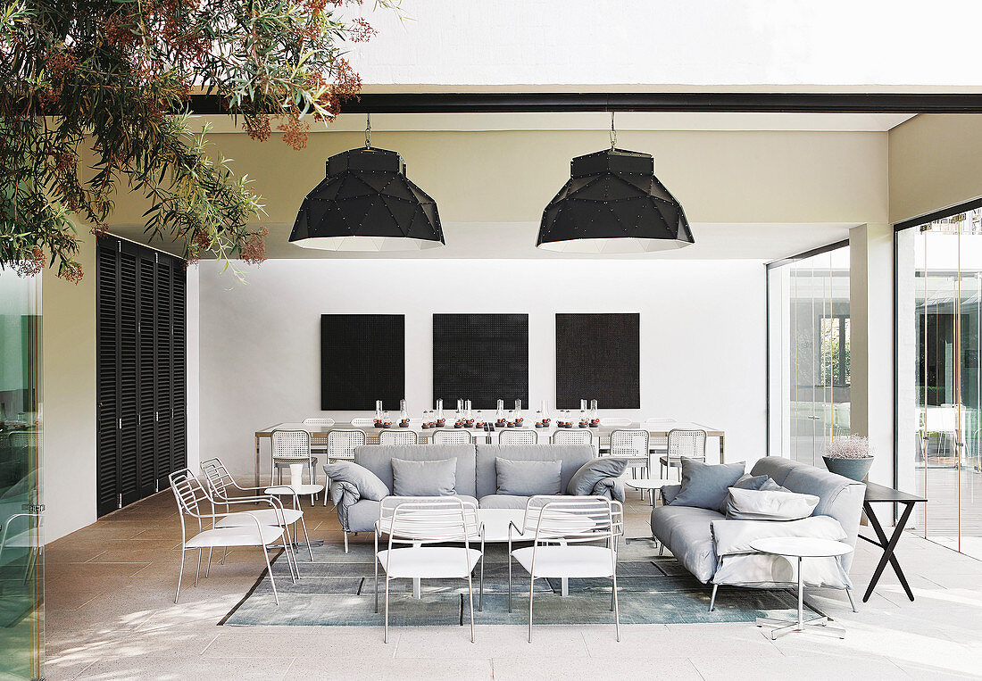 White and pale grey furniture in lounge area with long dining table in background