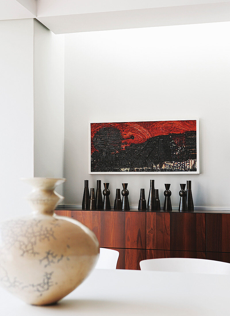 Black vases on exotic-wood sideboard below artwork on wall