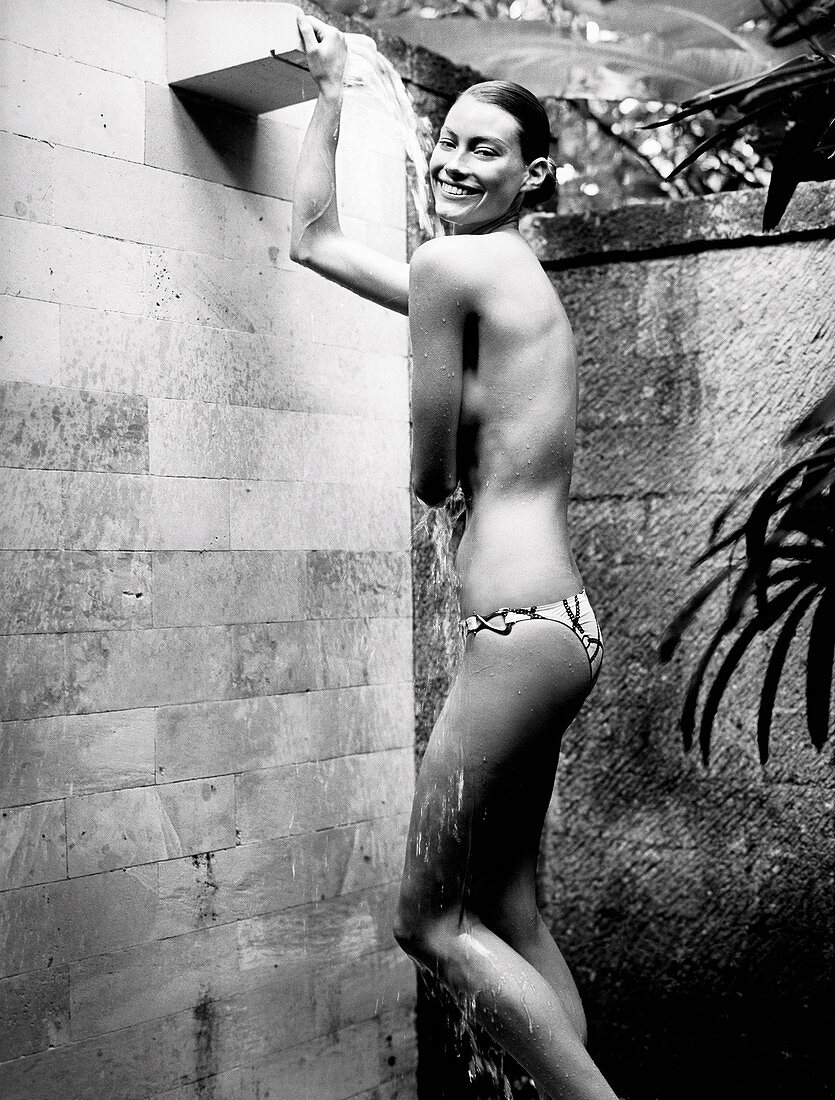 A young woman wearing bikini bottoms under an outdoor shower (black-and-white shot)