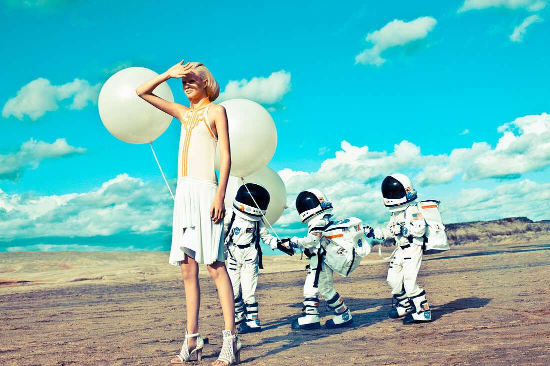 Futuristic Fashion: Blonde Frau und Kinder in Raumfahrer-Anzug mit Luftballons im Freien