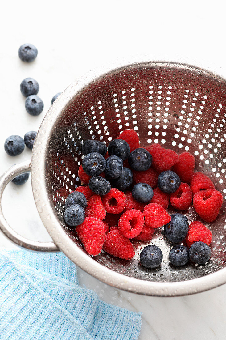 A colander with blueberries and raspberries