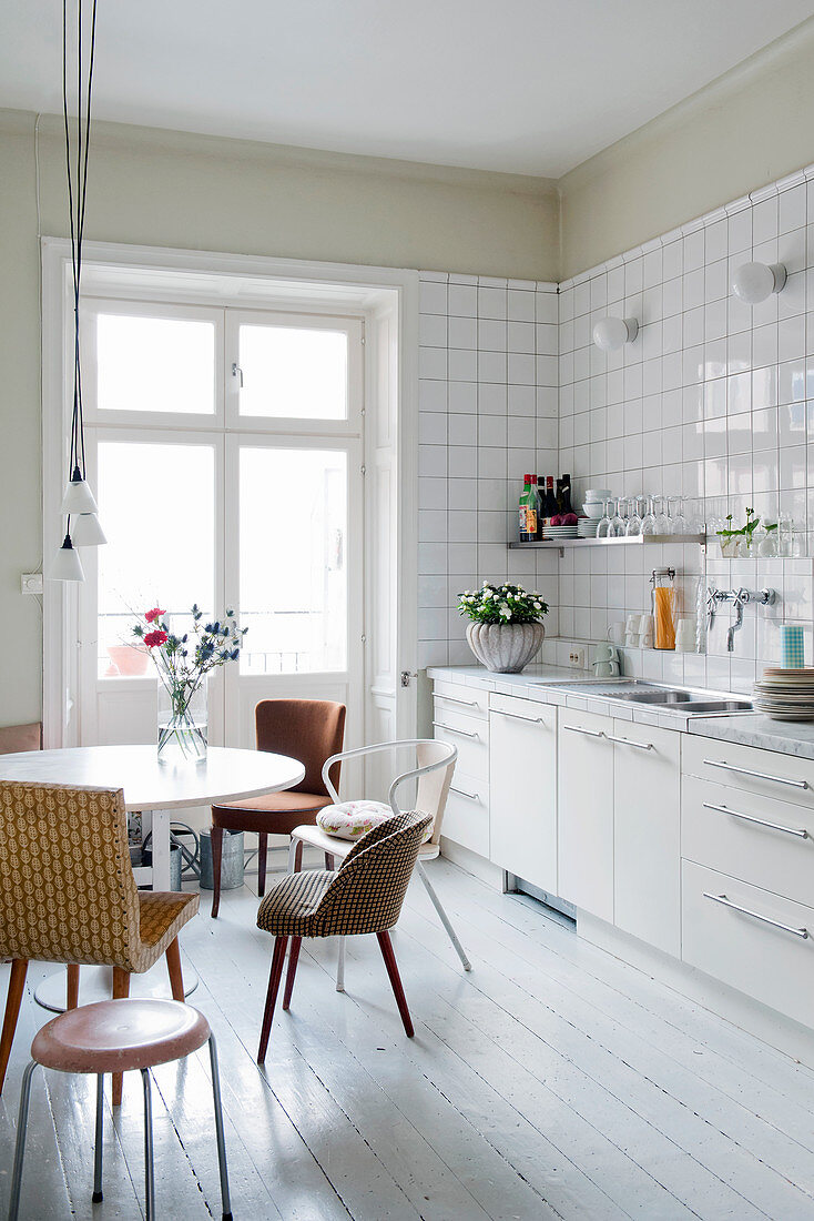 Various retro chairs at round table next to white kitchen counter