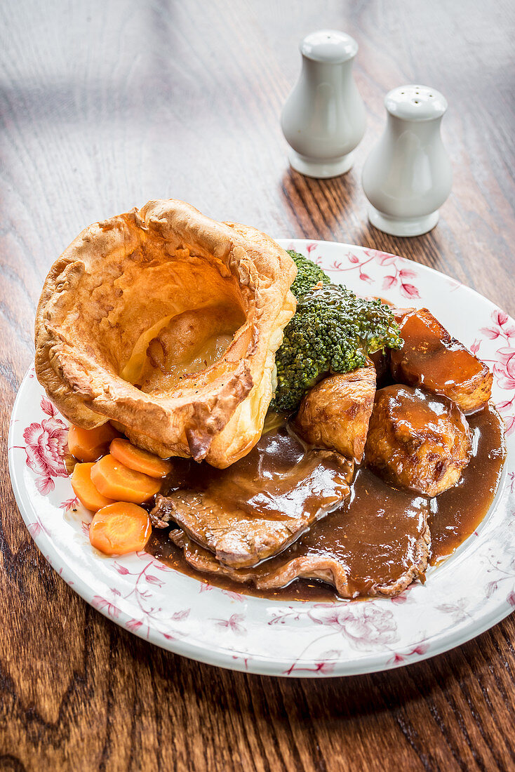 Complete Sunday roast platter with sliced roast beef, carrots, broccoli, potatoes, yorkshire pudding and a mountain of gravy