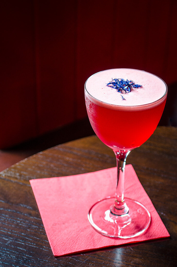 Red cocktail decorated with cornflowers on a red napkin and wooden table