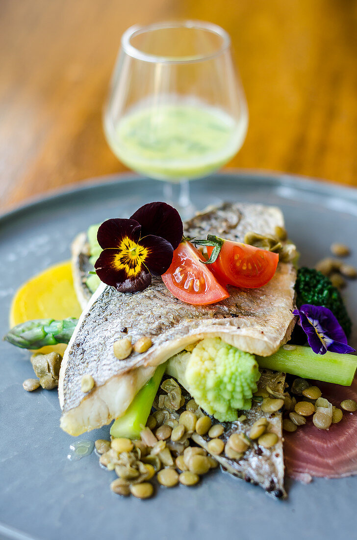 Pan fried sea bass fish fillet on a lentil, broccoli, beetroot, asparagus, tomatoes and edible flowers salad