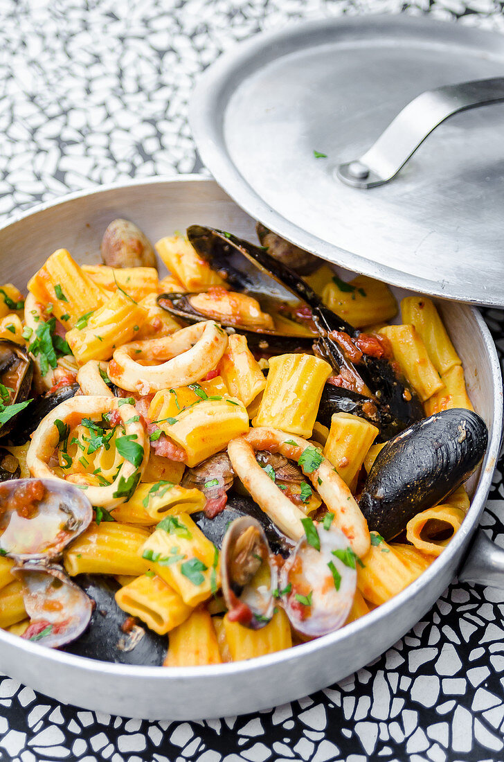 Mezze maniche rigatoni pasta with seafood, calamari, squid, mussel, clams, cockles, parsley, tomato sauce