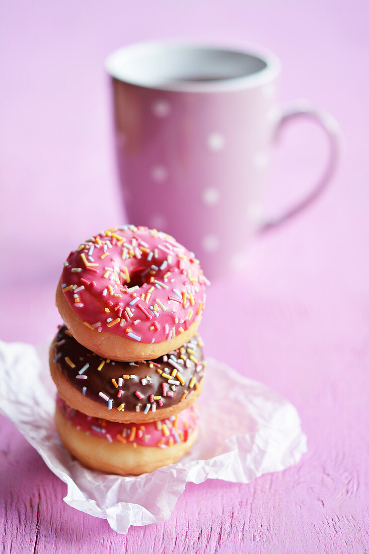 Drei gestapelte Mini-Donuts mit Glasur und Zuckerstreuseln vor Teetasse
