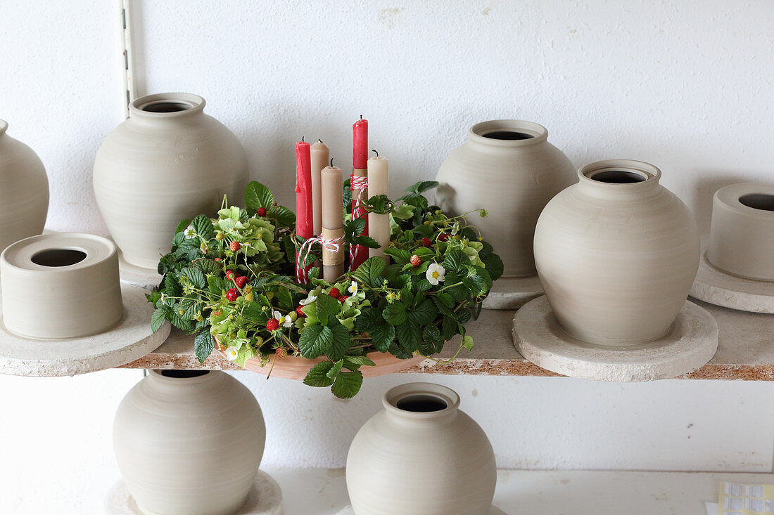 Candles in wreath of strawberry plants surrounded by clay pots