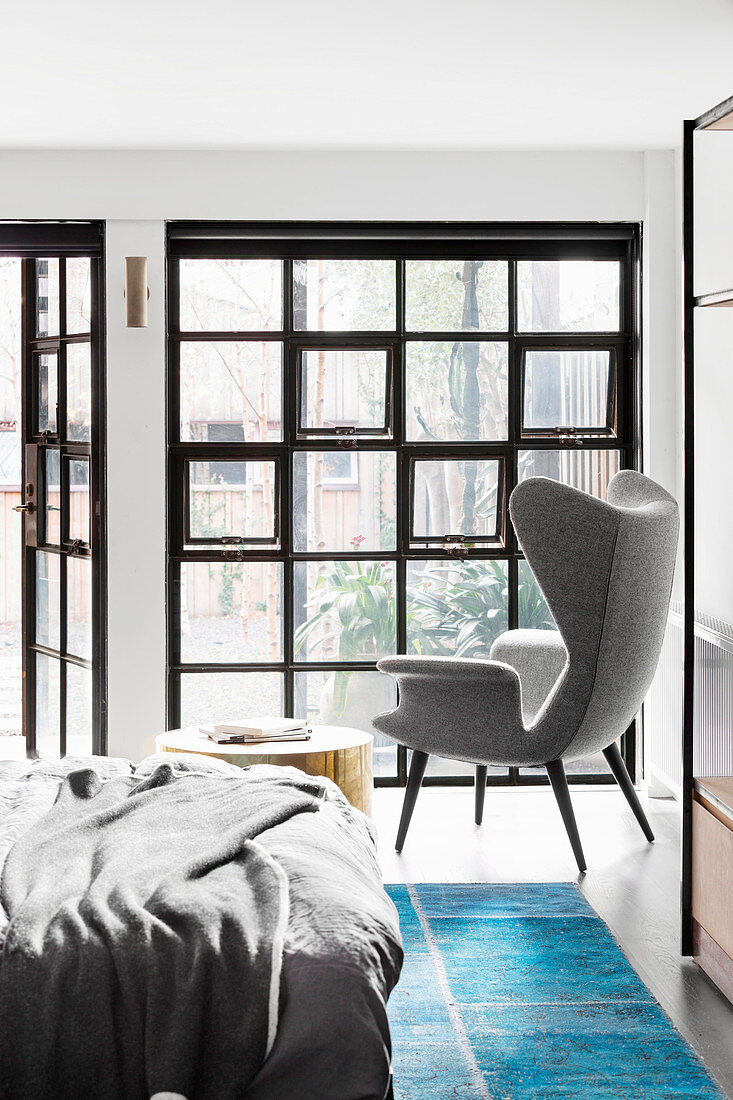 Double bed, side table and wing chair in the bedroom with industrial window