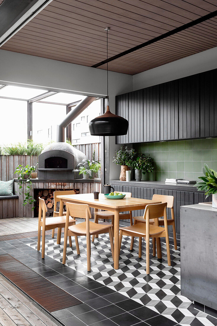 Black kitchenette with green wall tiles and dining area, pizza oven on the terrace in the background