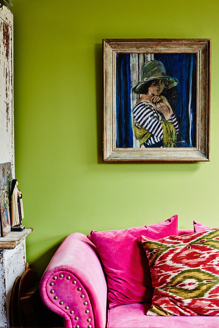 Painting of woman on green wall above hot-pink sofa