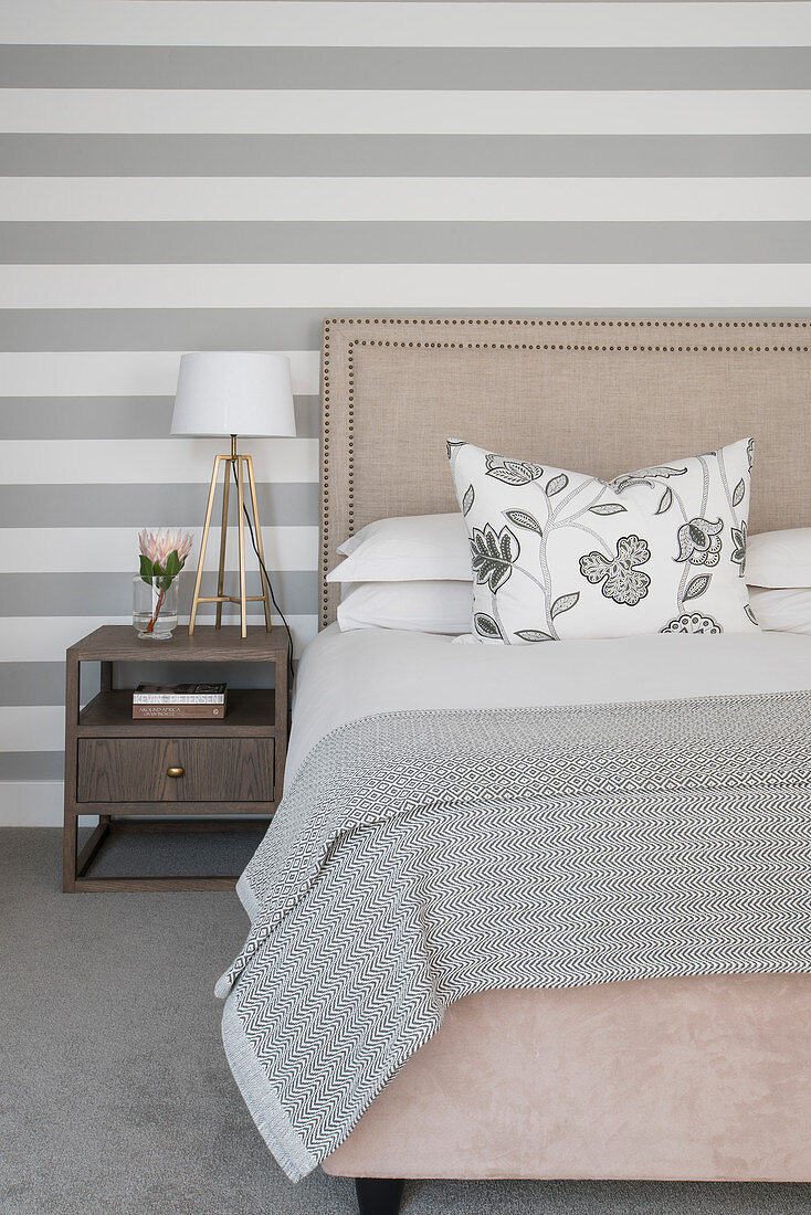 Doppelbett und Nachttisch vor grau-weiß gestreifter Tapete im Schlafzimmer