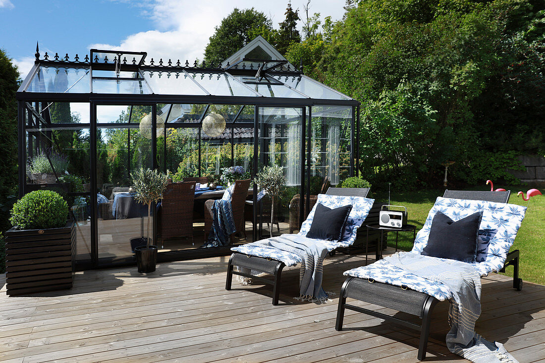 Zwei Liegen auf sonnigem Holzdeck vor Wintergarten