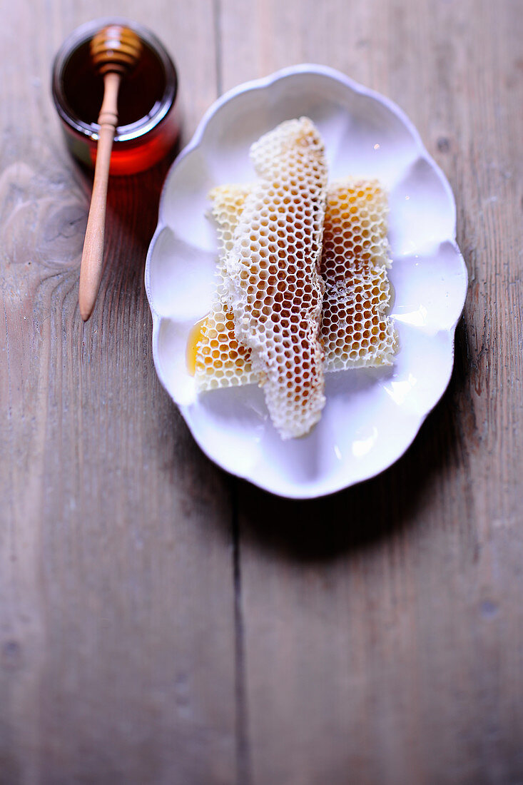 Pieces of honeycomb on a plate and a jar of honey with a dipper resting on top of it