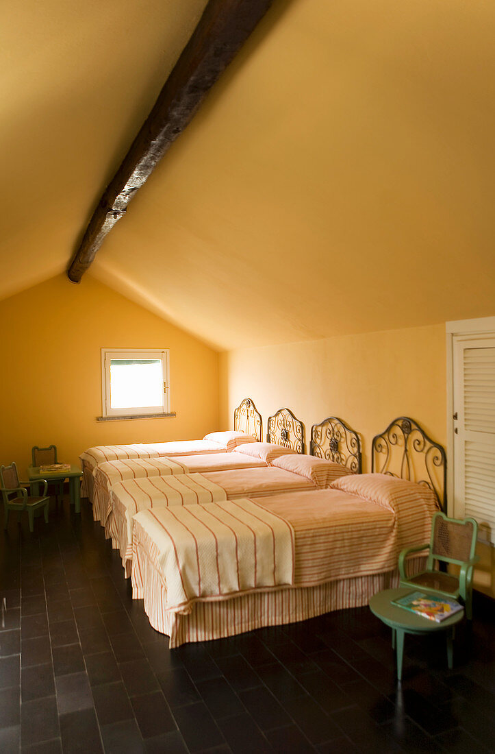 Four wrought iron single beds in attic room with black-tiled floor