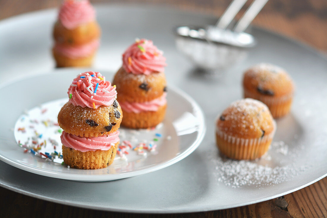 Kleine Muffins mit Tortencreme, Puderzucker und Zuckerstreuseln