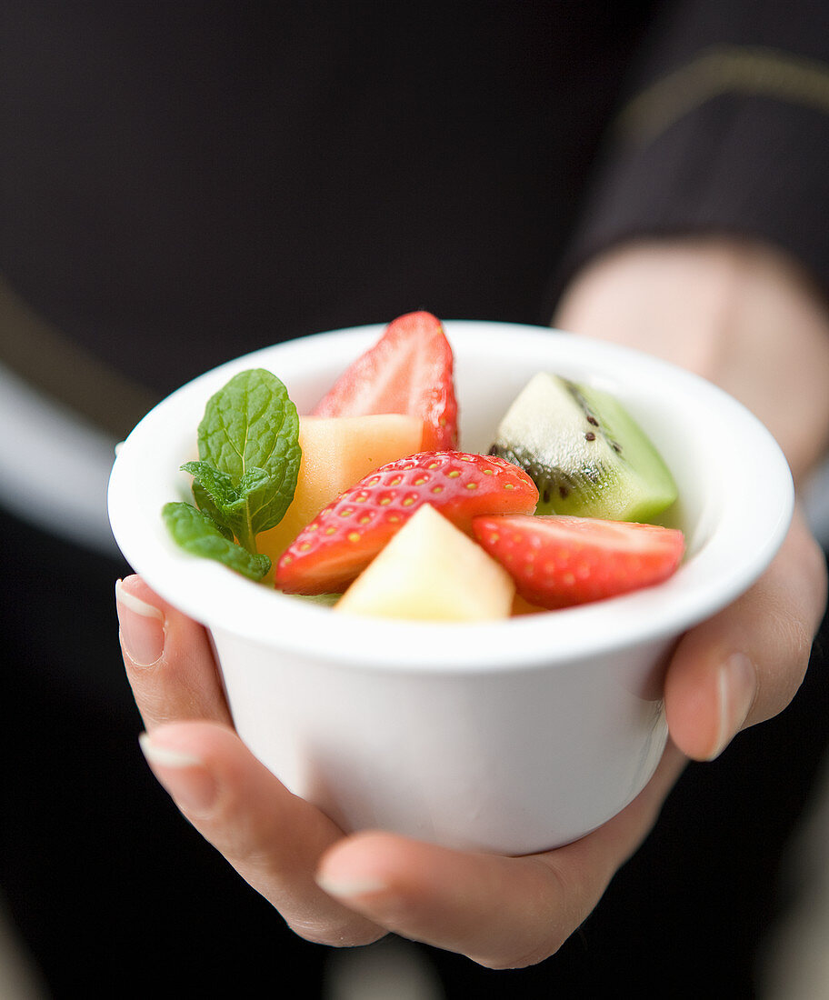 Hand holding a small white ball with mixed fruit salad