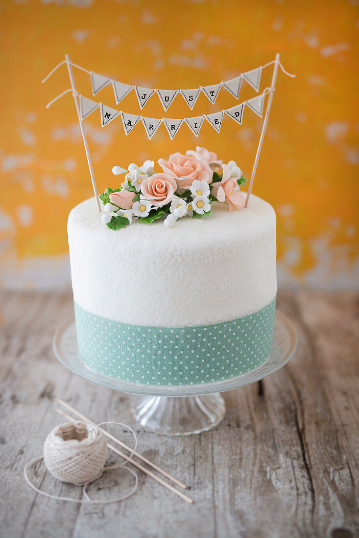 A wedding cake with sugar flowers, a ribbon and a 'Just Married' bunting decoration