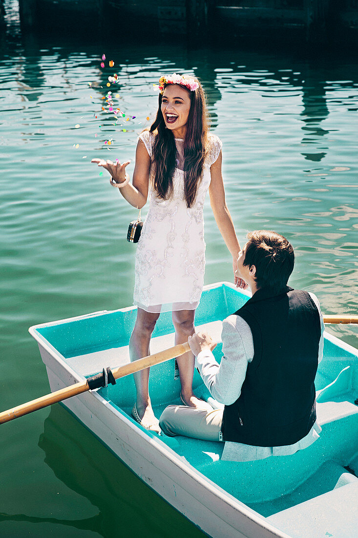 A girl wearing an elegant white dress and a floral headdress and boy wearing a waistcoat and a jacket in a boat