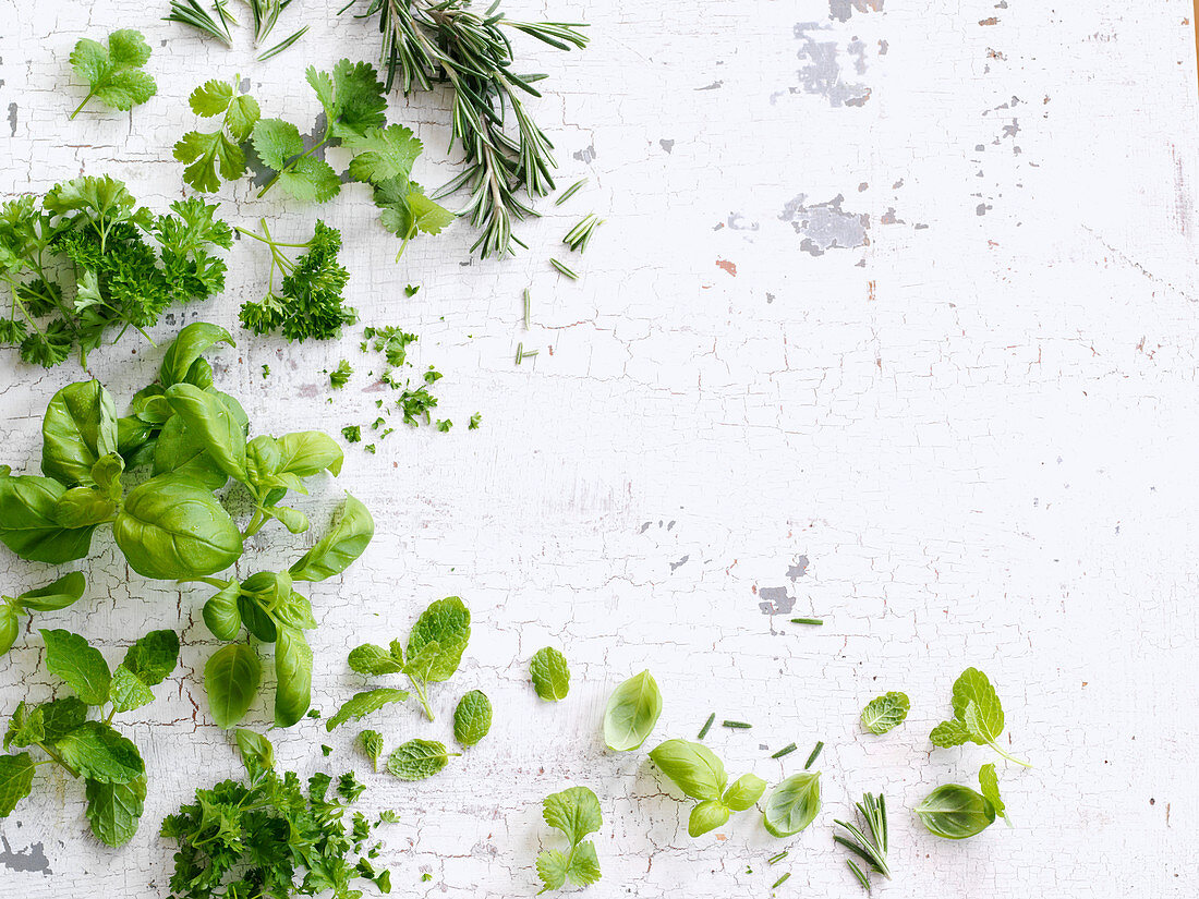 Various fresh kitchen herbs on a white wooden background (top view)