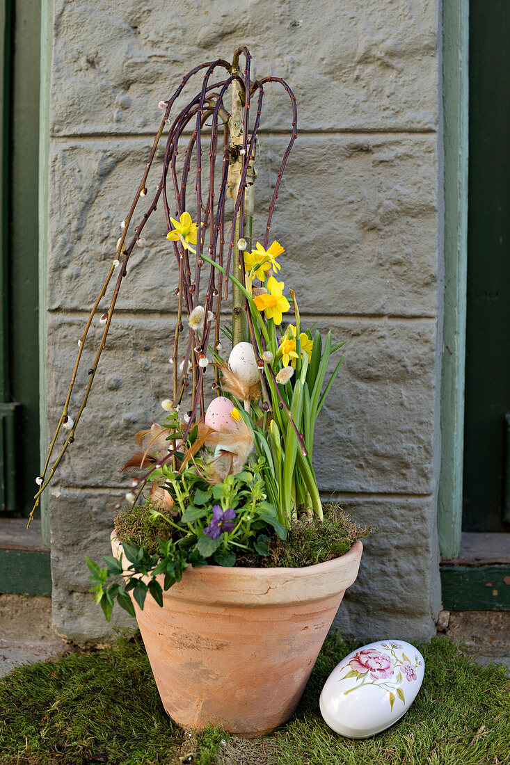 A decorative plant pot in front of a house with willow branches and daffodils