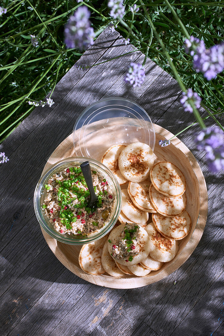 Blinis with trout rillette served outdoors on a wooden table (top view)